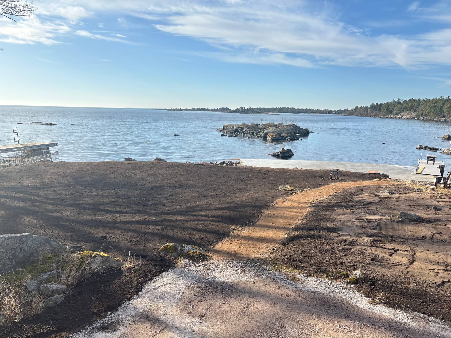 Nylagd matjord och grusgång på en kusttomt mot hav, brygga och skärgård