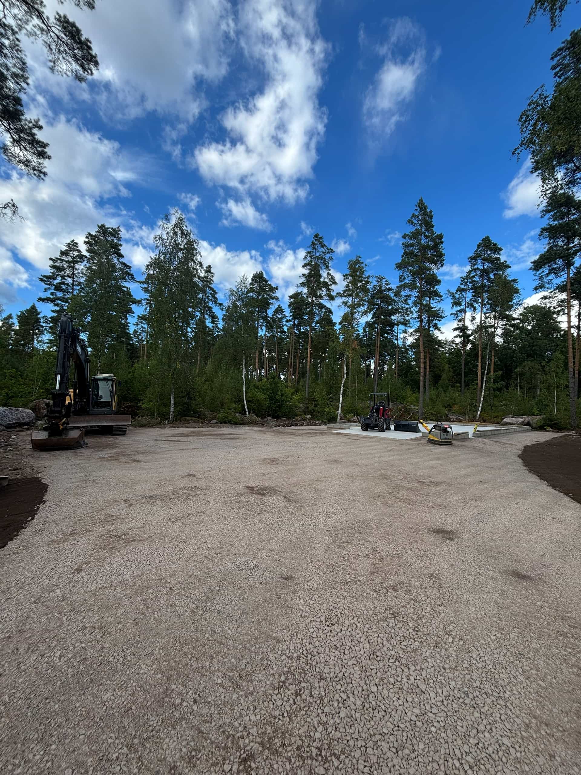 Färdig grusyta med grävmaskin på en tomt i skogsmiljö