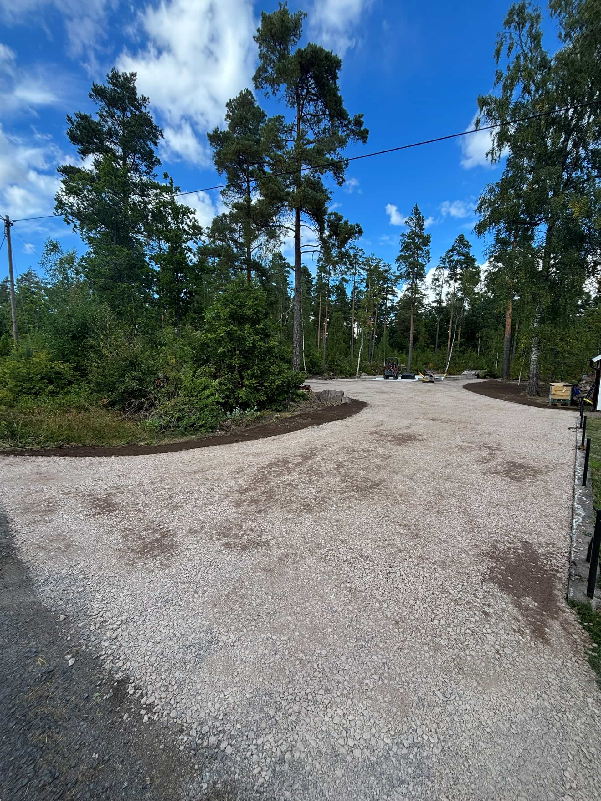 Nyanlagd grusinfart vid röd förrådsbyggnad och skog