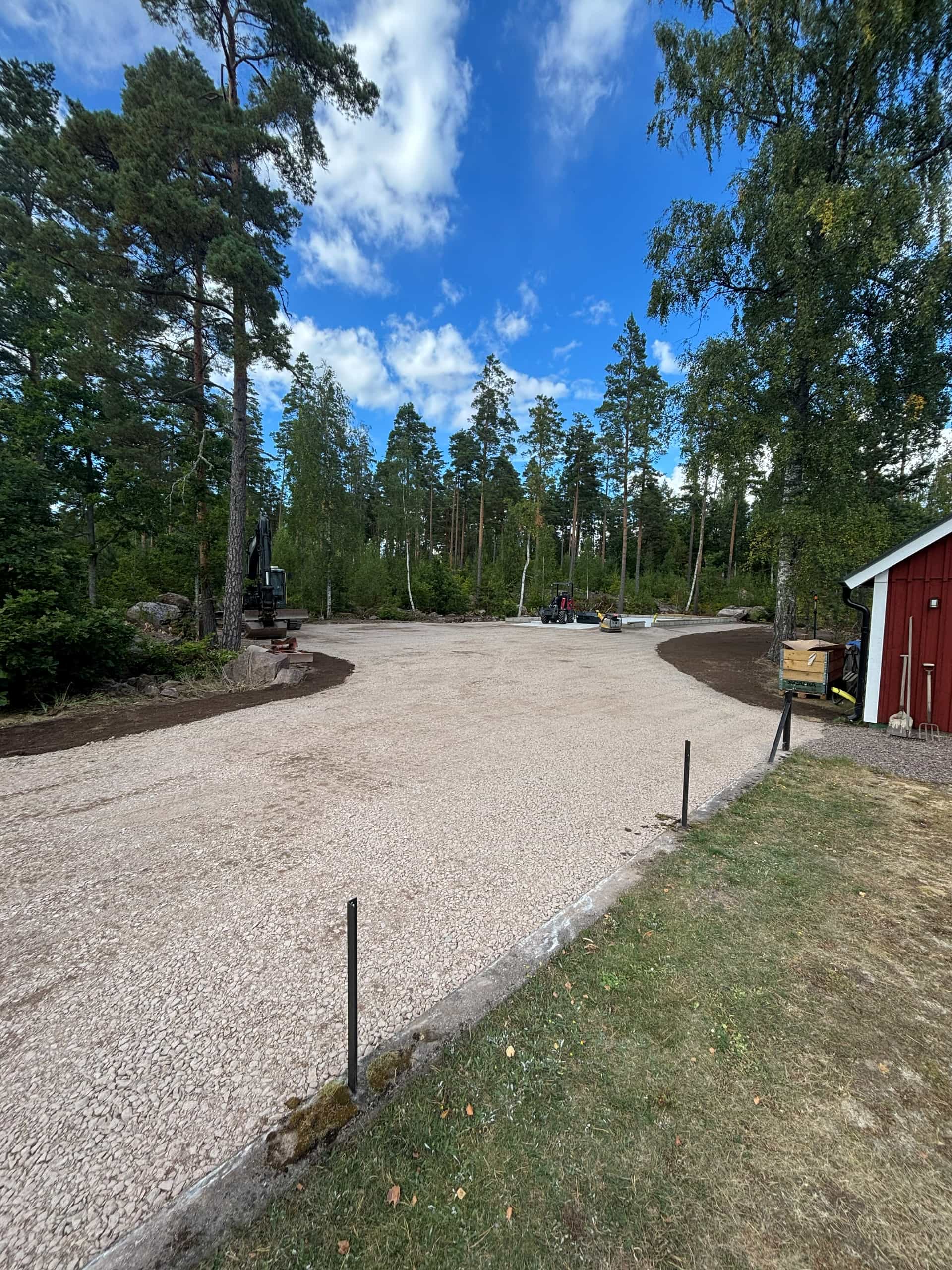 Nyanlagd grusyta runt röd förrådsbyggnad i skogsmiljö