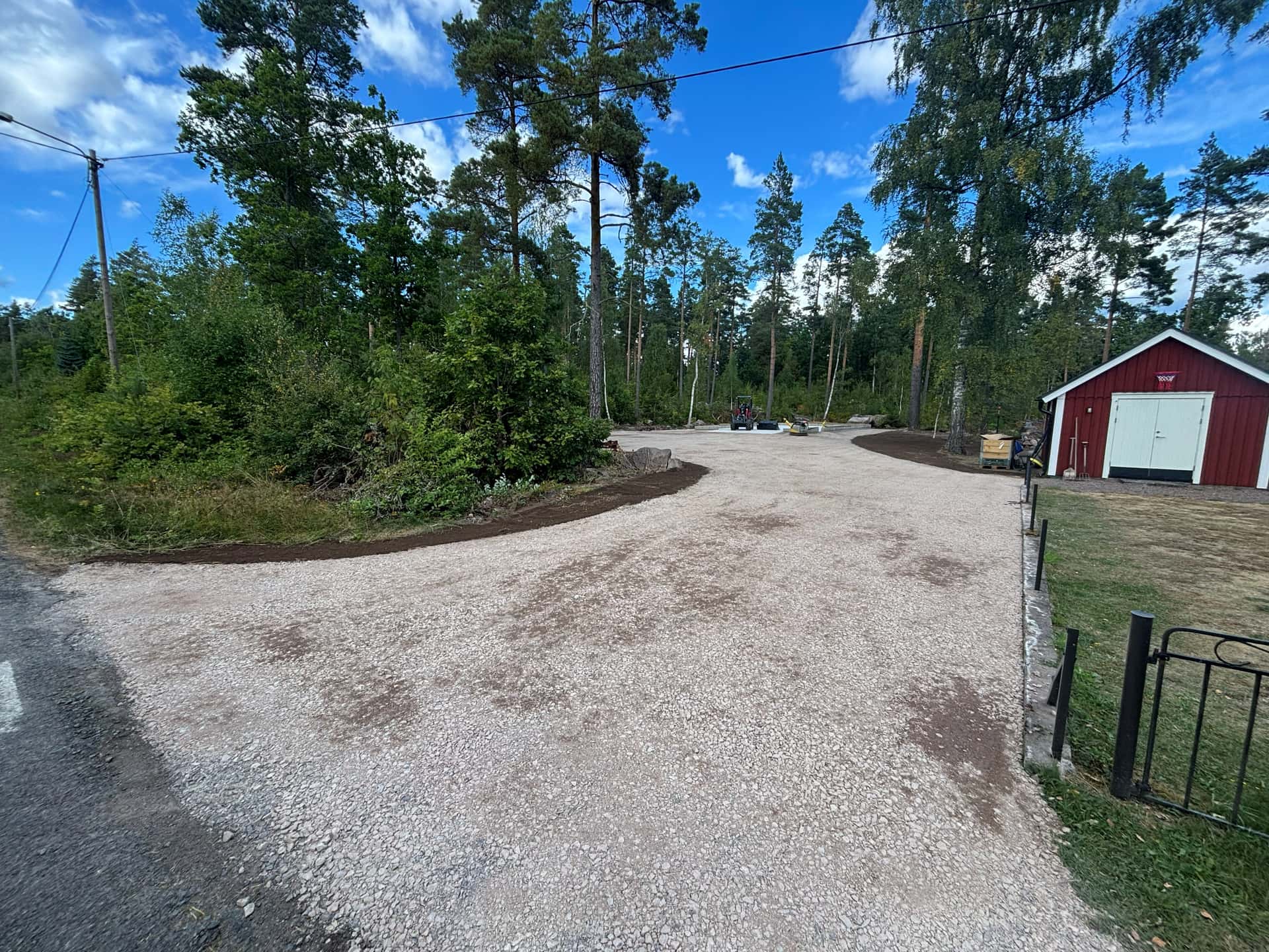 Färdig grusinfart vid röd förrådsbyggnad i skogsmiljö