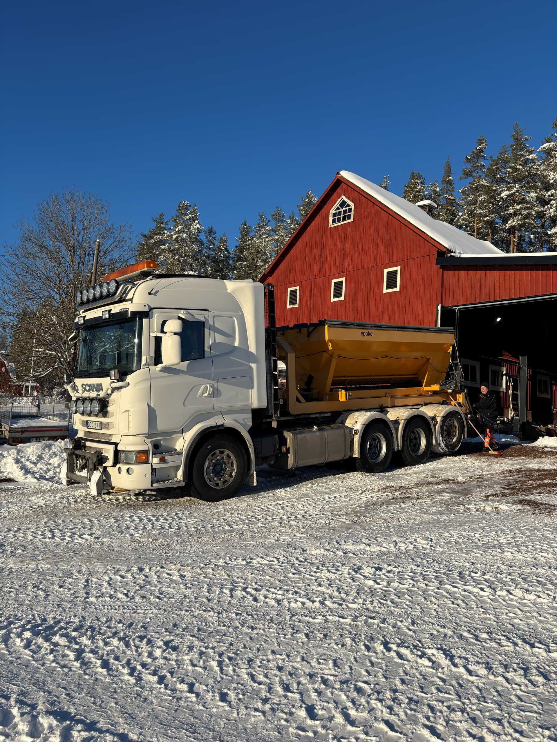 Lastbil med utrustning för vintervägunderhåll på en snötäckt gårdsplan